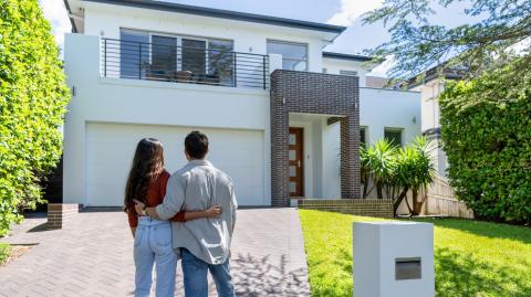 Un jeune couple enlacé admire la maison neuve qu'il vient d'acquérir