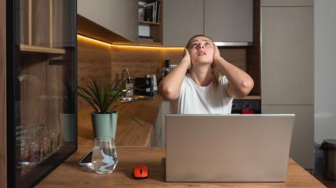 Une jeune femme travaillant sur son pc portable se bouche les oreilles en regardant le plafond de son appartement