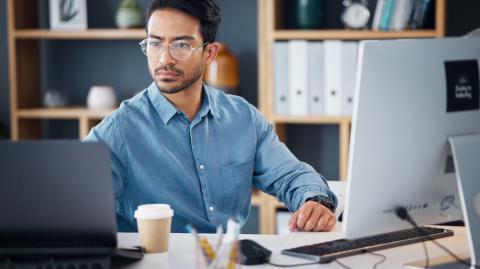 Un homme brun portant des lunettes fait des recherches sur son ordinateur de bureau