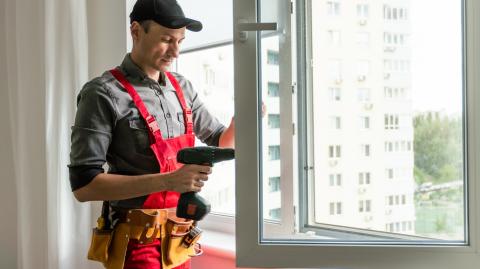 Un artisan, en salopette et casquette, installe un nouveau vitrage sur la fenêtre d'un logement