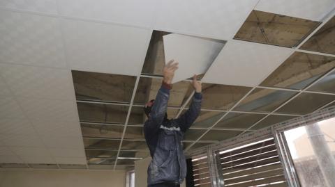 Un ouvrier pose des dalles sur des rails dans le cadre de la réalisation d'un faux-plafond