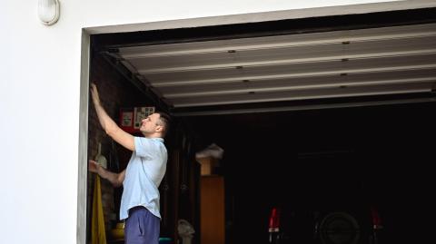 Un homme vérifie une installation dans son garage ; la porte de son garage est ouverte en grand
