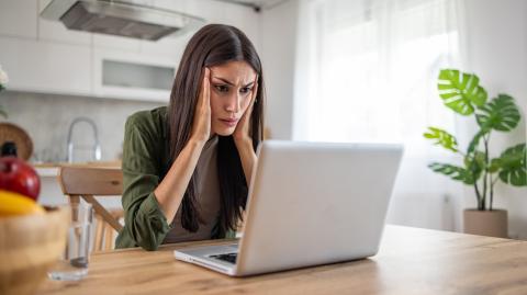 Une femme brune aux cheveux longs se tient la tête dans ses mains devant son pc portable, soucieuse