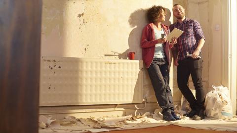 Un couple adossé contre un mur regarde avec satisfaction l'appartement qu'il est en train de rénover