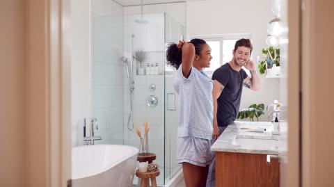 Un homme et une femme en pyjama se sourient devant le miroir de leur magnifique salle de bain