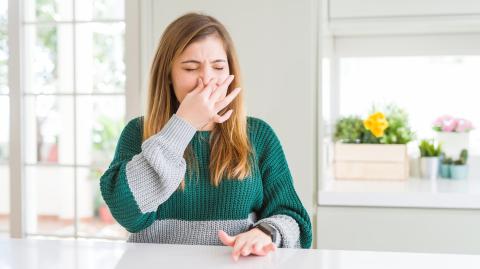 Une jeune femme se bouche le nez, en grimaçant, gênée par une mauvaise odeur