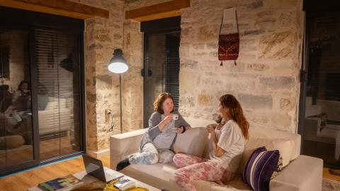 Deux femmes en pyjama discutent dans le salon, confortablement installées sur un canapé placé devant un mur en pierres