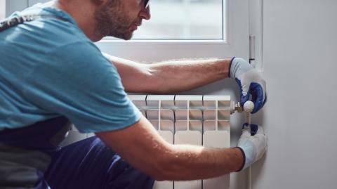 Un chauffagiste en bleu de travail effectue l'entretien d'un radiateur mural
