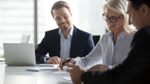 Une femme blonde signe un contrat chez le notaire, avec un grand sourire