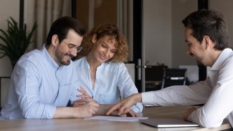 Un jeune couple signe des documents, guidé par son notaire