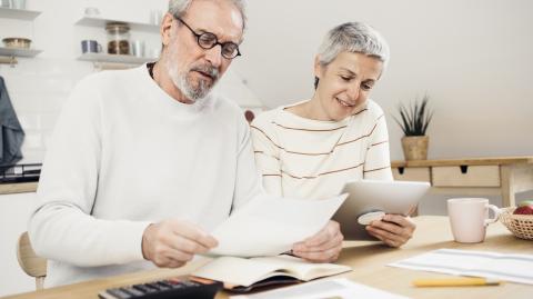 Un couple d'âge mûr assis à une table réalise une étude, à l'aide d'une tablette et d'une calculatrice