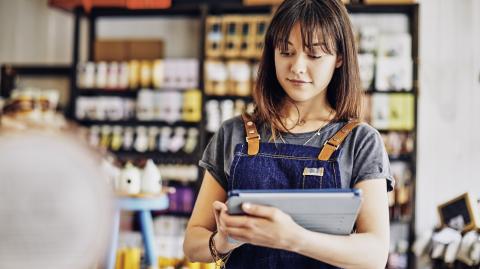Une jeune entrepreneure portant une salopette en jean travaille à l’aide de sa tablette numérique dans son épicerie fine