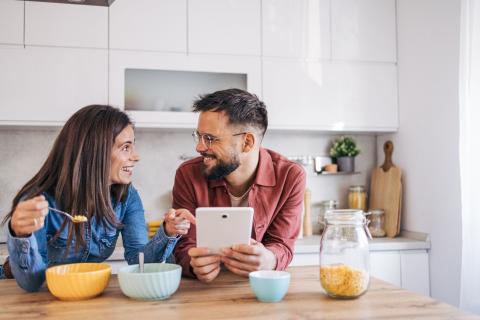 Couple déjeune en lisant leur sur leur tablette la mine réjouie