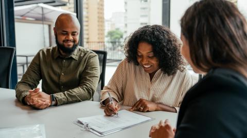 Un couple signe un contrat avec une jeune femme qui représente le promoteur immobilier en charge de la construction de leur maison