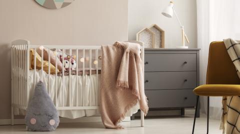 Une chambre d'enfant dans les tons roses avec un lit de bébé et une commode grise