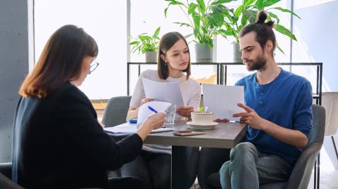 Un jeune couple étudie des documents au cours d'un rendez-vous avec une professionnelle de l'immobilier