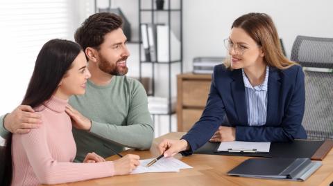 Un jeune couple consulte les documents remis par son notaire au cours d'un rendez-vous pour la signature d'un acte de vente