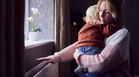 Une maman tenant son bébé dans les bras passe la main au-dessus du chauffage mural pour voir s'il fonctionne