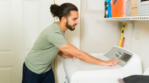 Un jeune homme d'origine hispanique programme son lave-linge dans sa buanderie