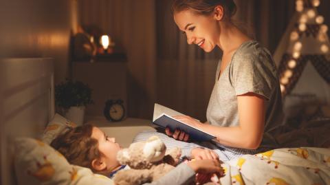 Une maman, assise sur le lit de son petit garçon, lui lit une histoire avant qu'il s'endorme