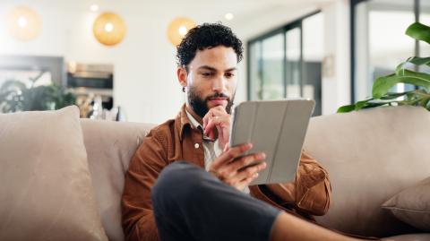 Un homme assis sur son canapé consulte des informations sur une tablette