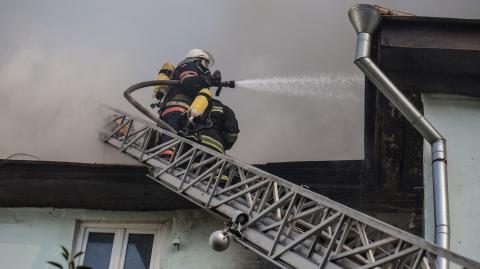 Un pompier professionnel projette un produit avec sa lance pour éteindre un incendie dans un logement depuis une échelle d'intervention