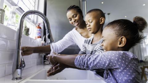 Une maman aide ses deux enfants qui se lavent les mains ensemble au lavabo de la salle de bain