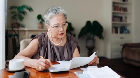 Une femme d'âge mûr vérifie ses factures sur sa table de salon, à l'aide de sa calculatrice