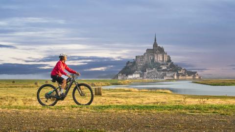 Touriste à vélo devant le Mont Saint-Michel, emblème de la Manche
