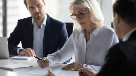 Une femme d'affaires signe un contrat en présence de deux hommes en costume