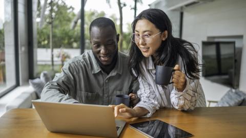 Un jeune couple complète un questionnaire en ligne sur un pc portable dans son salon