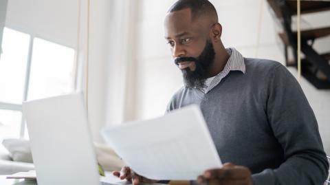 Un homme étudie des documents sur son pc portable, un document à la main