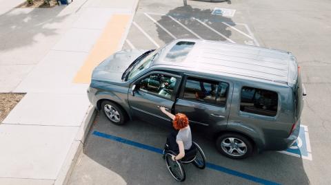 Une femme se déplaçant en fauteuil roulant ouvre la portière avant de son véhicule garé sur une place handicapé