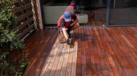 Un homme passe une couche de produit au pinceau sur une terrasse en bois pour la protéger et lui redonner de l'éclat