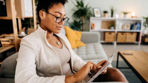 Une femme assise sur son canapé consulte un dossier sur sa tablette