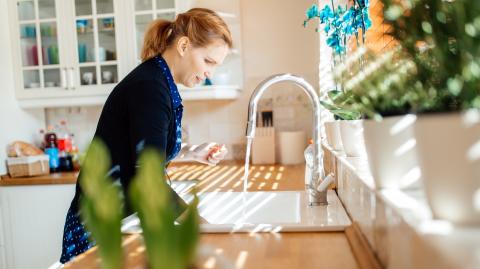 Une femme debout dans sa cuisine fait couler de l'eau dans son évier 