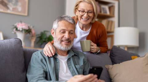 Un couple de retraités regarde des informations sur un téléphone portable dans son salon