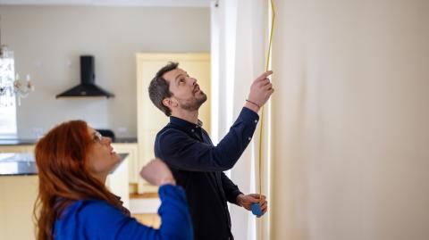 Un couple mesure la hauteur d'un mur de son logement à l'aide d'un mètre