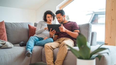 Un couple, dont la femme est enceinte, effectue des recherches sur tablette, installé sur son canapé