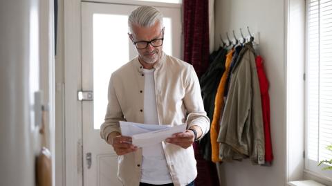 Un homme aux cheveux blancs lit un courrier qu'il vient de recevoir à son domicile