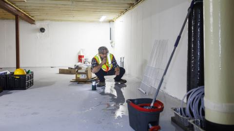 Un homme accroupi recherche les causes d'une inondation dans un sous-sol