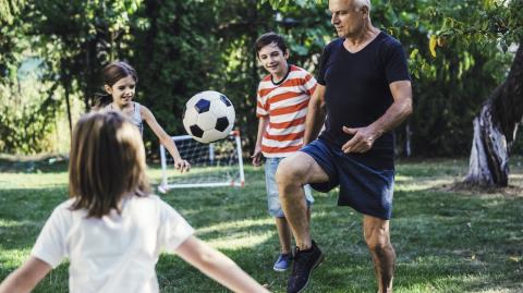 Des enfants jouent au foot dans leur jardin avec un homme d'âge mûr