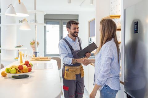 Une femme reçoit un ouvrier dans sa belle cuisine claire et lui serre la main. 