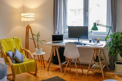 Chambre d'étudiant avec bureau, ordinateurs, fauteuil jaune et lampadaire allumé. 