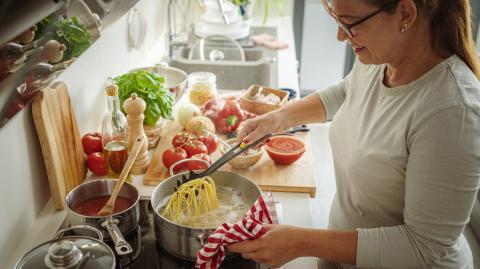 Une femme fait cuire des pâtes dans une grande casserole d'eau dans sa cuisine