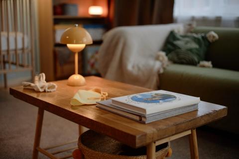 Petit appartement avec focus sur la table basse en bois brut, quelques livres et une lampe moderne jaune. 