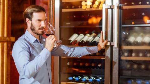 Un homme déguste un vin qu'il vient de choisir dans sa cave à vin réfrigérée