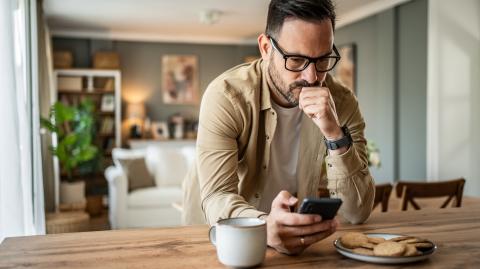 Un homme assis à la table de la cuisine apparait contrarié en lisant un message sur son téléphone