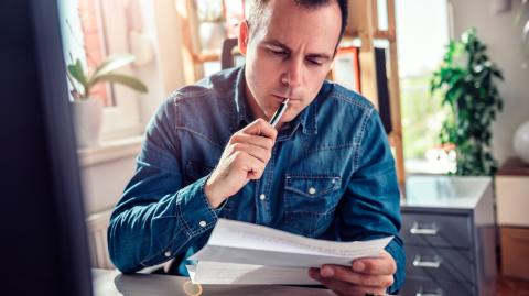 Un homme assis à son bureau vérifie avec attention le contenu du courrier qu'il tient dans la main