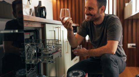 Un homme accroupi à côté de son lave-vaisselle admire la brillance de ses verres
